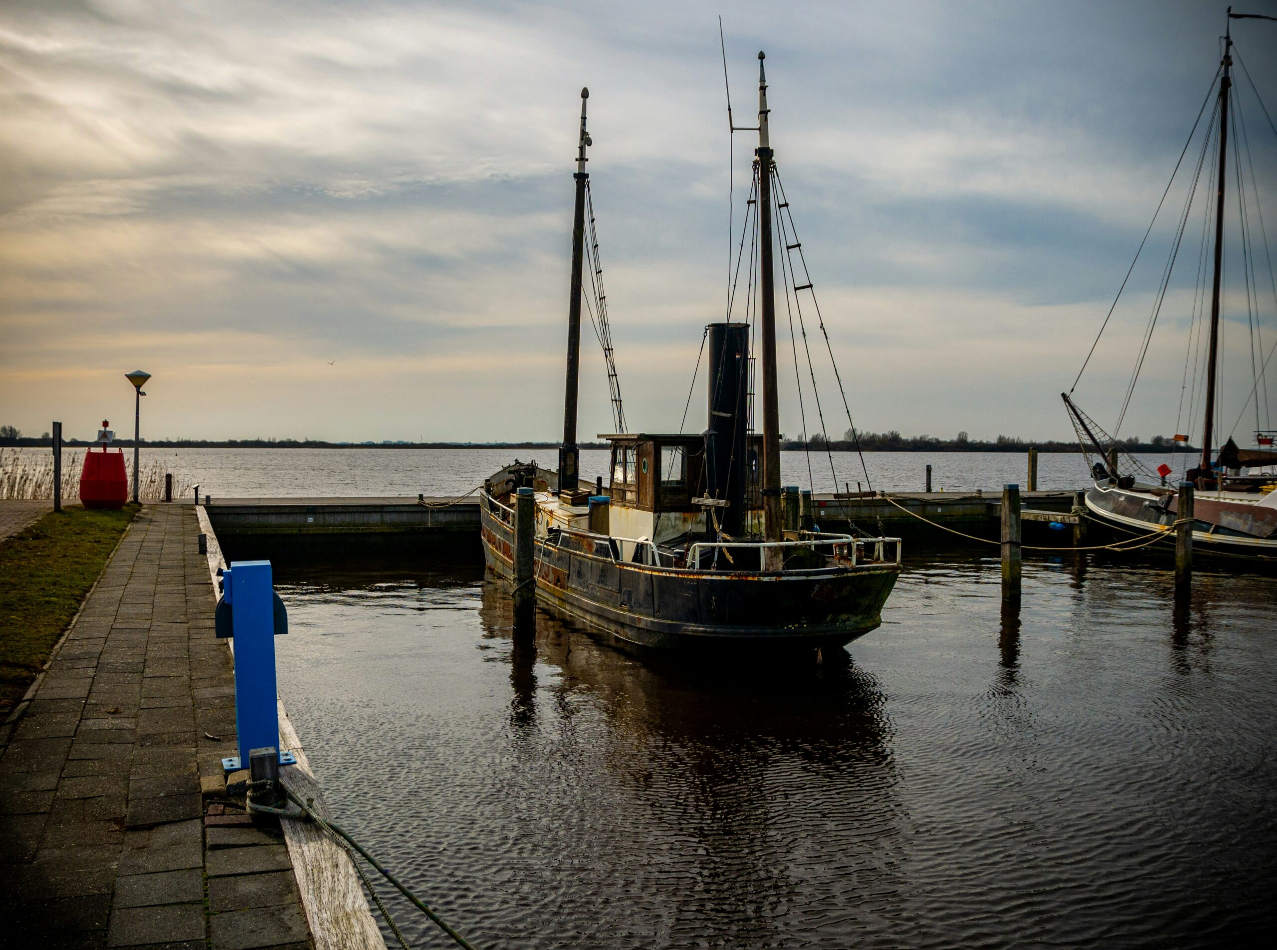 Oude houten vissersboot afgemeerd aan een steiger in de haven van Lauwersoog bij schemering
