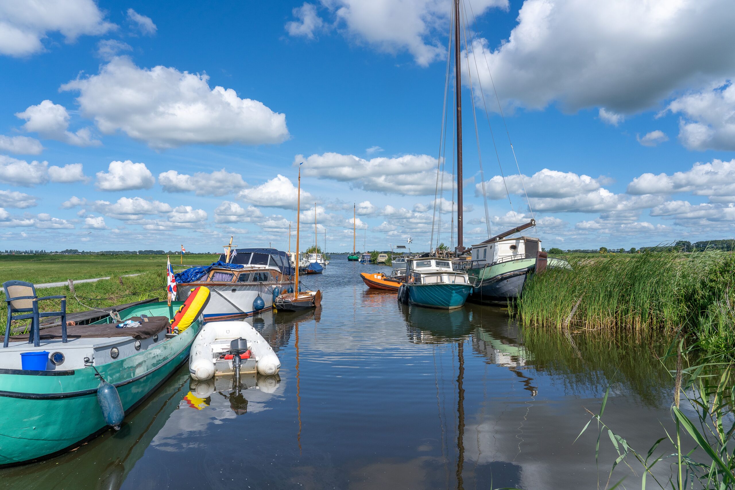 Traditionele platbodems en zeilboten afgemeerd in een rietkraag langs het water bij Zoutkamp, onder een lucht met stapelwolken