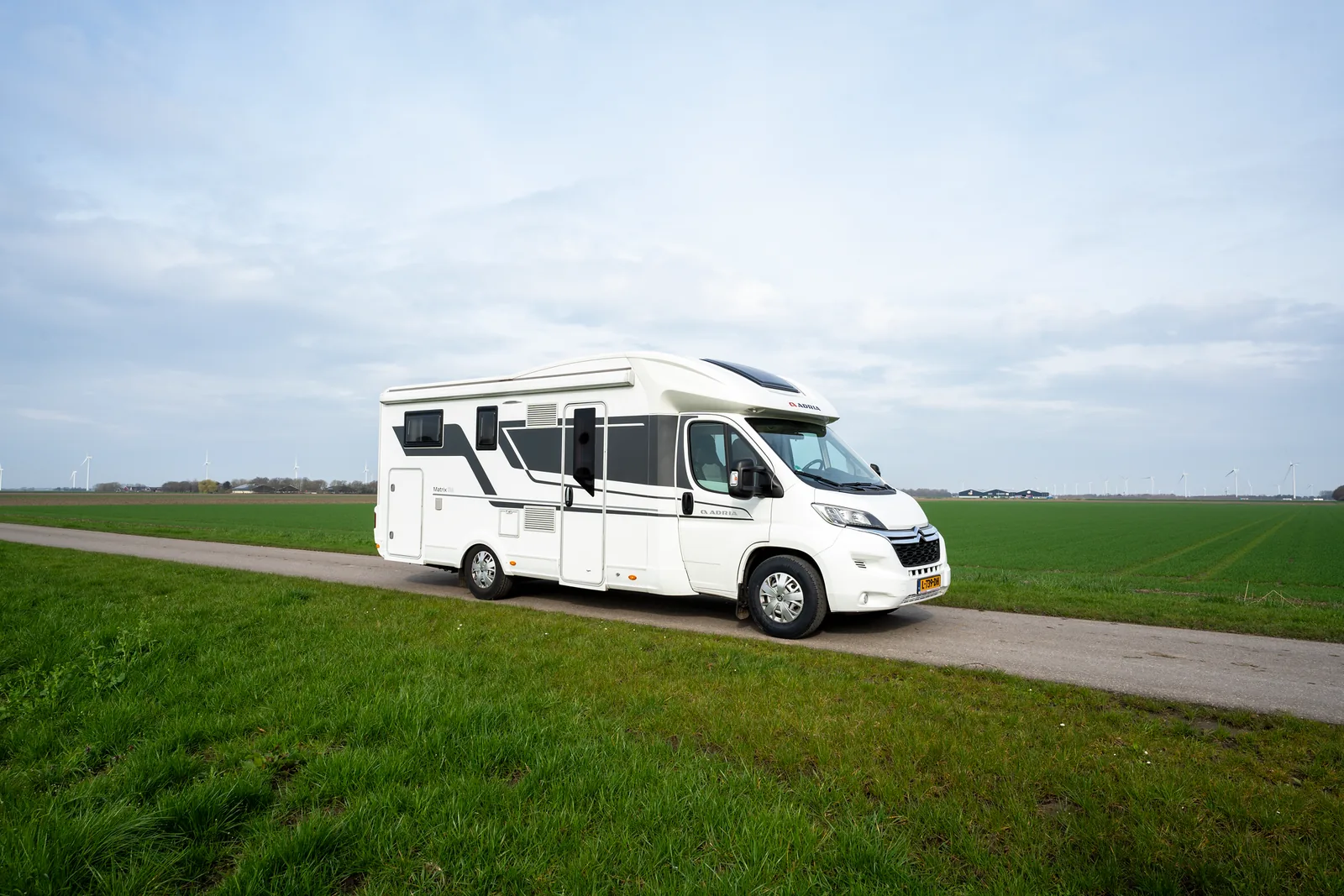 Halfintegraal camper Adria Matrix 670 SL van opzij, geparkeerd langs een weiland